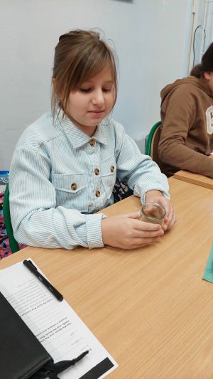 Uczniowie siędzą w ławkach i wykonują eksperymenty